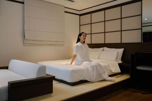 a woman sitting on a bed in a room at Aank Ryokan Hotel Suwon in Suwon