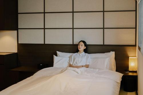 a woman sitting on a bed with pillows at Aank Ryokan Hotel Suwon in Suwon