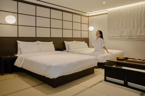 a woman sitting between two beds in a hotel room at Aank Ryokan Hotel Suwon in Suwon