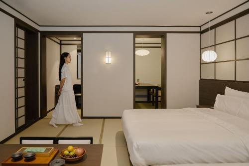 a woman walking through a hotel room with a bed at Aank Ryokan Hotel Suwon in Suwon