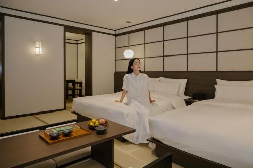 a woman sitting on two beds in a hotel room at Aank Ryokan Hotel Suwon in Suwon