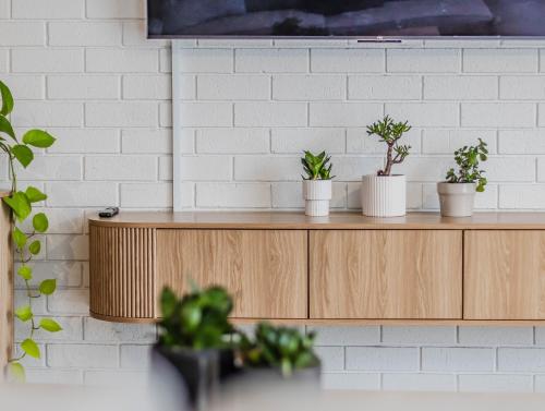 a white brick wall with three potted plants on a wooden shelf at Ultimate Beachside Haven in Cabarita - Pet Friendly in Cabarita Beach