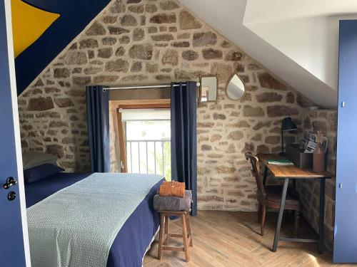 - une chambre dotée d'un mur en pierre avec un lit et un bureau dans l'établissement Gîtes d Izel2 entre terre et mer prés d'un golf, à Ploemel