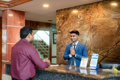 a man standing at a counter talking to another man at Hotel Presidency Kempegowda International Airport Bangalore in Devanahalli-Bangalore