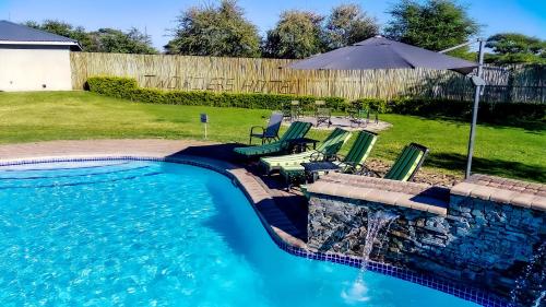 a swimming pool with two lawn chairs and an umbrella at Two Rivers Hotel in Kasane