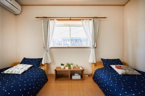 東京にあるUU Houseのベッド2台とテーブルと窓のある寝室