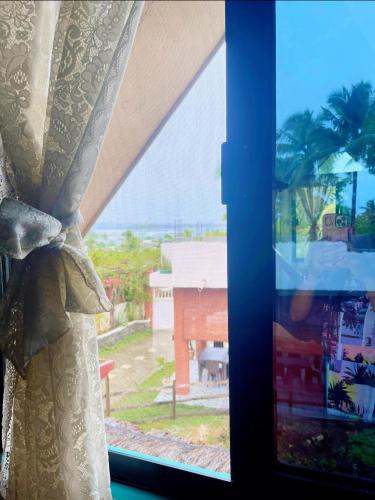 a window with a curtain and a view of a house at Casa De Moore - Ocean & Garden View Siargao in General Luna
