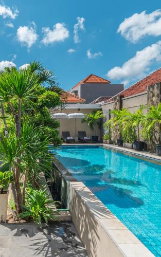 a swimming pool with palm trees next to a building at Svarna Suites Seminyak in Seminyak