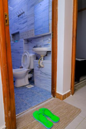 a bathroom with a toilet and a sink and a pair of slippers at Happy Home Ke in Meru