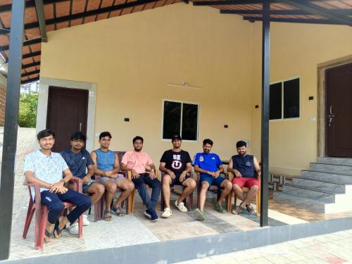 a group of men sitting on chairs in front of a house at HALASE HOMESTAY in Mudigere