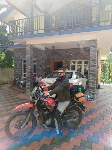 a man sitting on a motorcycle in front of a house at HALASE HOMESTAY in Mudigere