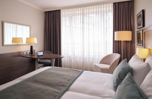a hotel room with a bed and a desk and a window at Leonardo Royal Hotel Düsseldorf Königsallee in Düsseldorf