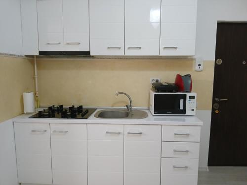 a kitchen with white cabinets and a sink and a microwave at DML Apartment in Mamaia Nord
