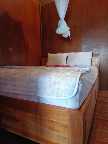 a bedroom with a wooden bed with white sheets at Lumbung House in Gili Gede
