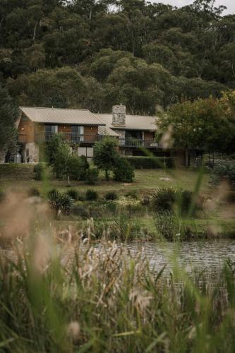 a house in the middle of a field next to a lake at Rooke River Lodge in Jindabyne