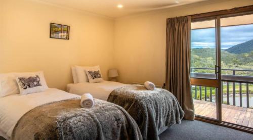 two beds in a room with a balcony at Rooke River Lodge in Jindabyne