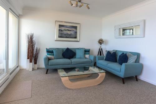 a living room with two blue couches and a table at Tides - Beach front apartment in Bracklesham Bay in Chichester