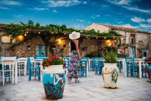 a woman in a dress standing in front of tables and chairs at The Sun 365 - Sea View Apartment in Portopalo