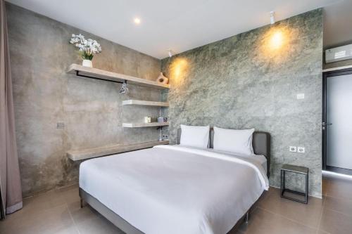 a bedroom with a white bed and a concrete wall at Brand new apartment with stunning sunset views in Munggu
