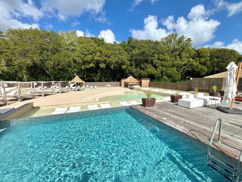 a swimming pool with chairs and a wooden deck at Sunset Dream, Bungalow haut de gamme avec accès Piscine et Plage in Grand-Bourg