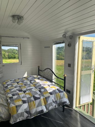a bedroom with a bed and two windows at Secret Valley Shepherds Hut in Llanfaenor