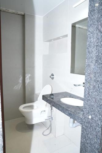 a white bathroom with a toilet and a sink at Hotel Yashraj Regency in Sangamner