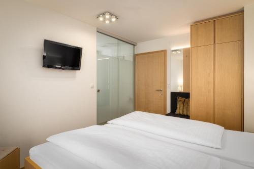a bedroom with a white bed and a tv on the wall at Hotel OXA - Easy Escape in Hittisau