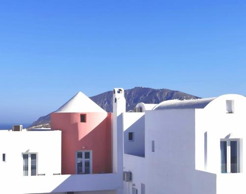 a group of white buildings with a mountain in the background at New Haroula in Fira