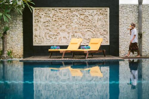 a man walking past two chairs and a swimming pool at The Casa Amaya in Jimbaran