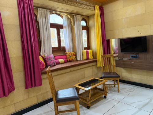 Una habitación con un asiento junto a la ventana con sillas y un televisor. en Hotel Zaza Jaisalmer, en Jaisalmer