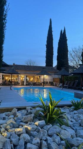 une grande piscine avec des rochers en face d'un bâtiment dans l'établissement Hôtel Spa Les Alpes, à Gréoux-les-Bains