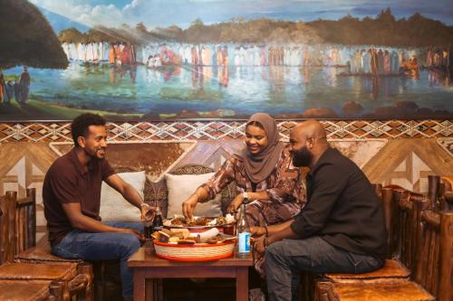 three people sitting around a table in front of a painting at Capital Hotel and Spa in Addis Ababa