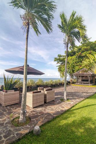 a patio with two palm trees and an umbrella at Beautiful Beach Villa Nujum with staff. in Lovina
