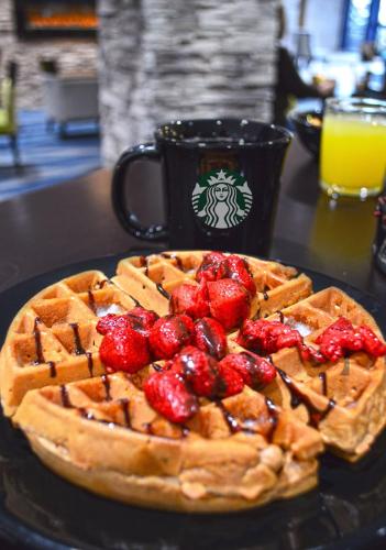 a waffle with strawberries on a table with a cup of orange juice at Holiday Inn & Suites Syracuse Airport - Liverpool by IHG in Liverpool