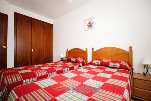two beds in a bedroom with red plaid sheets at Edificio Esmeralda in Peniscola