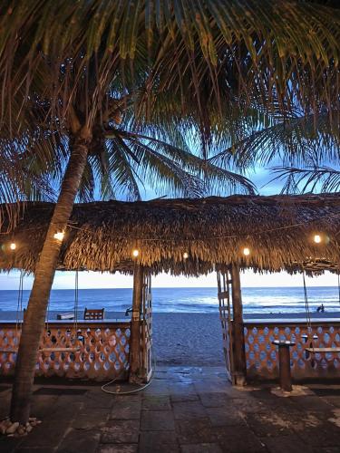 a beach with a straw umbrella and a palm tree at El Belga Loco in Las Peñitas