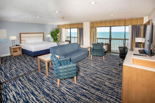 a hotel room with a bed and a couch and chairs at Wyndham Virginia Beach Oceanfront in Virginia Beach