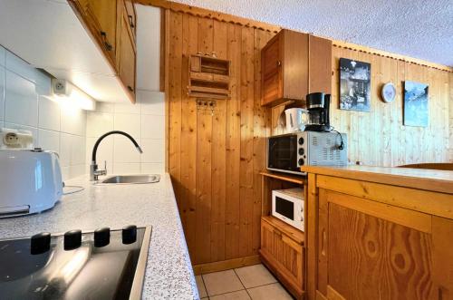 La cuisine est équipée de placards en bois, d'un évier et d'un four micro-ondes. dans l'établissement Résidence Courmayeur - Appartement 6 personnes ski aux pieds aux Ménuires MAE-3874, aux Menuires