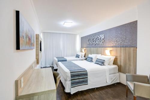 a hotel room with two beds and a table at Allia Gran Pampulha Suites in Belo Horizonte