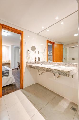 a bathroom with a large sink and a large mirror at Allia Gran Pampulha Suites in Belo Horizonte