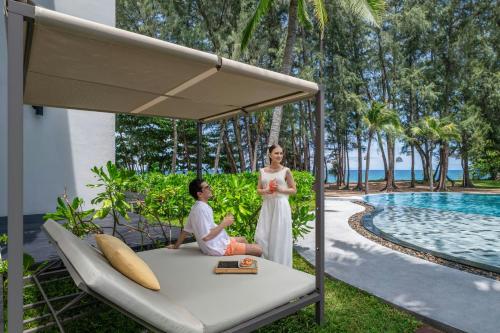 a woman standing next to a man sitting on a bed next to a pool at Le Meridien Phuket Mai Khao Beach Resort in Mai Khao Beach