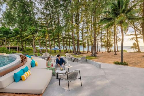 a couple sitting at a table by a pool at a resort at Le Meridien Phuket Mai Khao Beach Resort in Mai Khao Beach