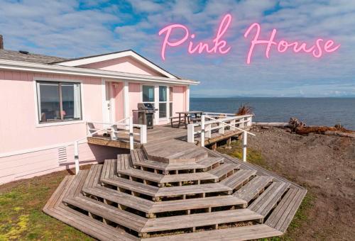 a pink house with a wooden deck next to the ocean at The Pink House - Dungeness Waterfront Home in Sequim