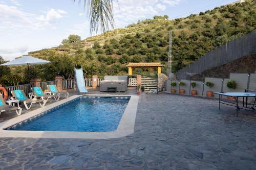 une piscine avec des chaises et une table et une colline dans l'établissement Cortijo de Carmen - Lujo Rustico en el Corazon de la Montaña, à Torrox