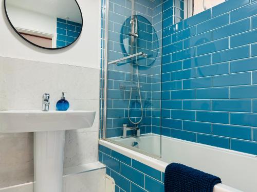 a blue tiled bathroom with a sink and a mirror at Two Bedroom Flat for Six Guests in London