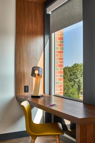 a desk with a lamp and a yellow chair next to a window at Aloft Raleigh in Raleigh