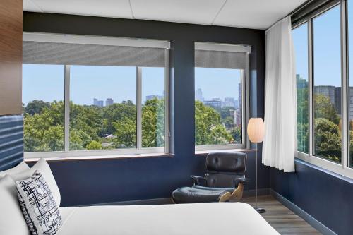 a bedroom with a bed and a chair and windows at Aloft Raleigh in Raleigh
