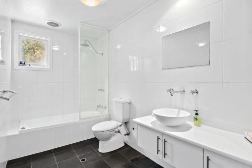 a white bathroom with a toilet and a sink at Bungala Cottage 28 Jetty Road in Normanville