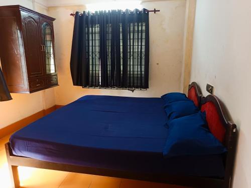 a bedroom with a bed with blue sheets and a window at Poonthanam guest house in Guruvāyūr
