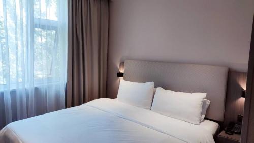 a bedroom with a bed with white sheets and a window at Hanting Hotel Beijing Temple of Heaven in Beijing